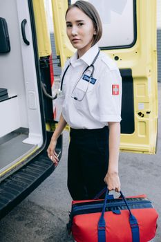 A female paramedic standing by an ambulance, carrying medical equipment. Represents emergency medical services.