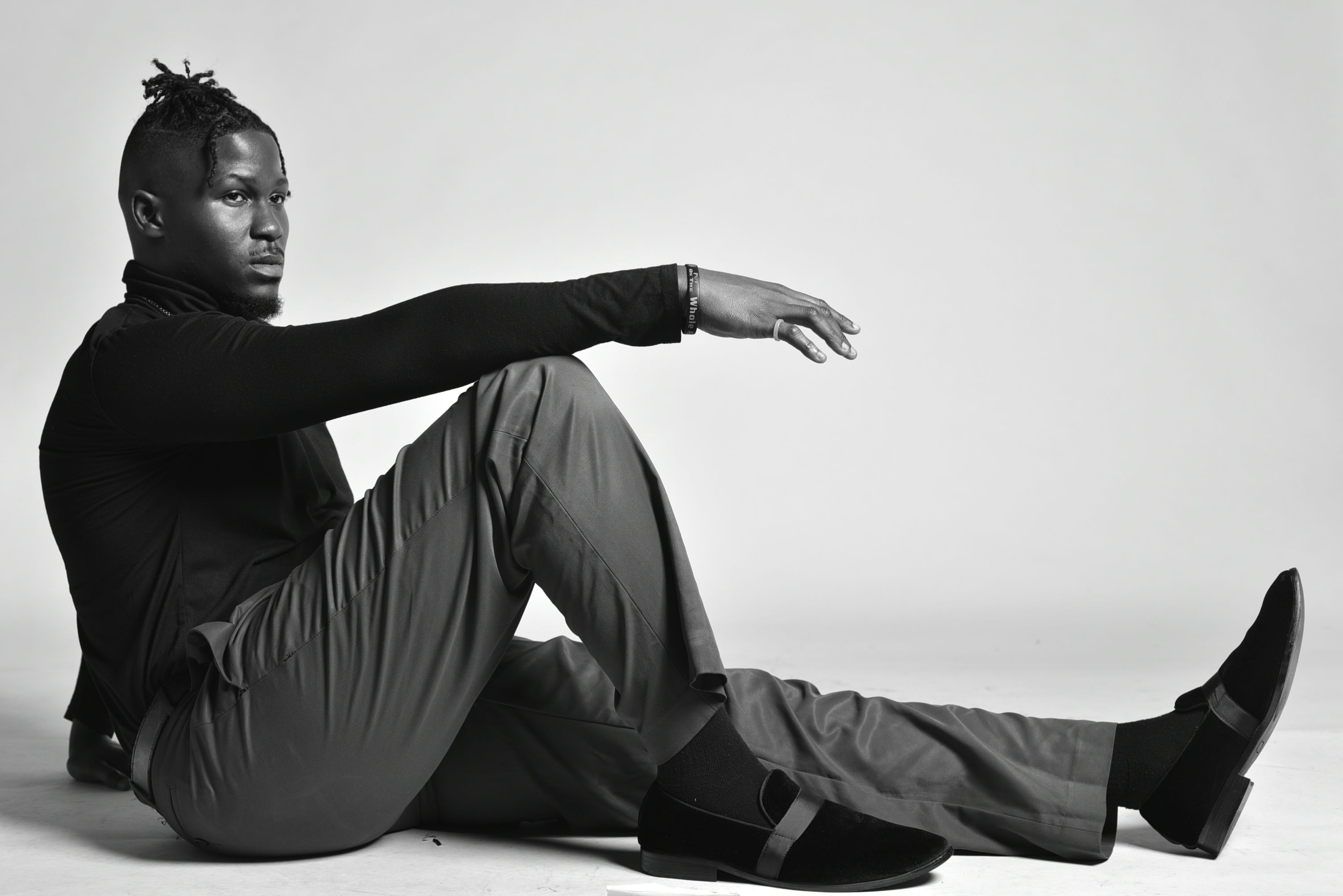 Black and white portrait of a stylish man sitting with an artistic pose in a studio setting.