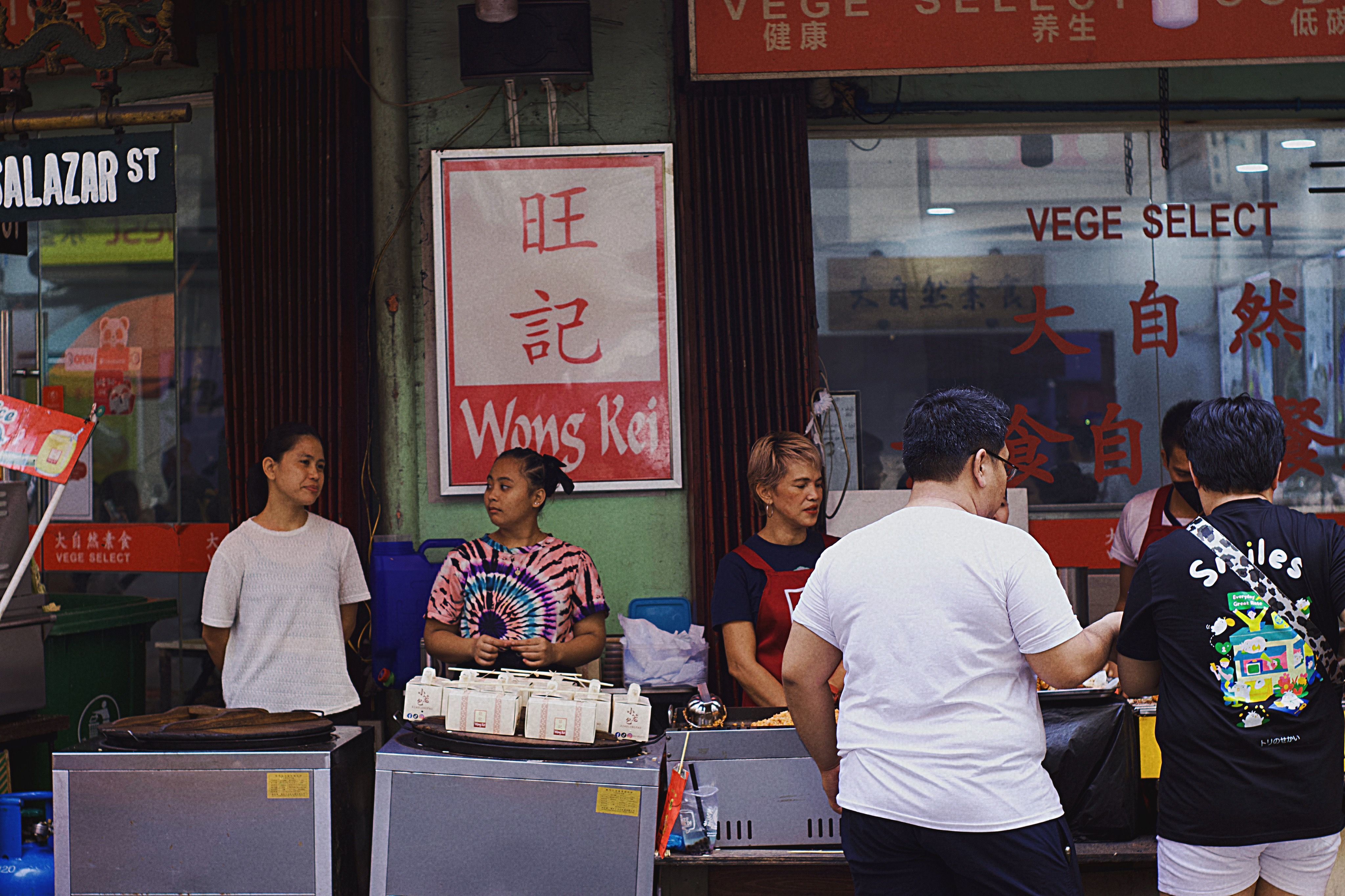 A lively street market scene with people interacting at food stalls, creating a vibrant, communal atmosphere.