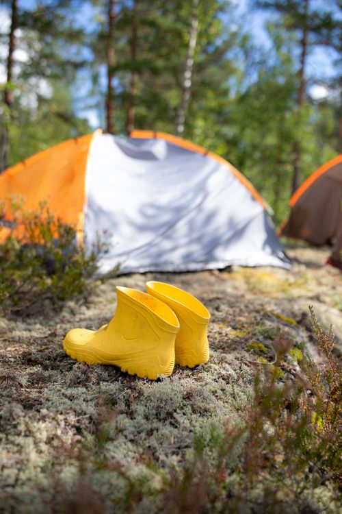 Free Bright yellow boots outside an orange tent in a lush wooded campsite, perfect for summer adventures. Stock Photo