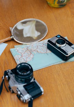 Two vintage cameras and a map on a wooden table, symbolizing travel and exploration.