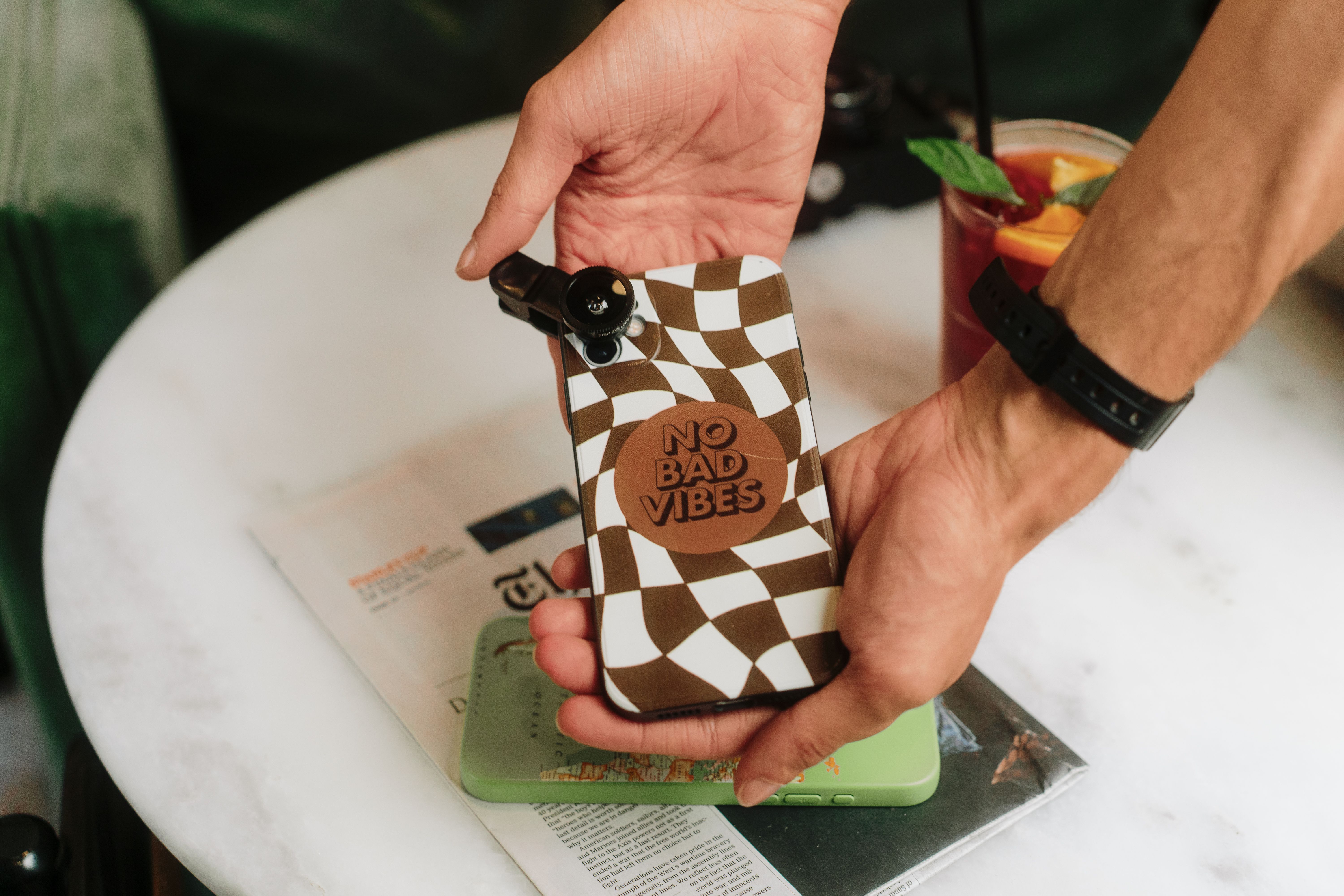 Brown and white checkered smartphone case with 'No Bad Vibes' message on table alongside drink. - High Quality Performance Evaluation