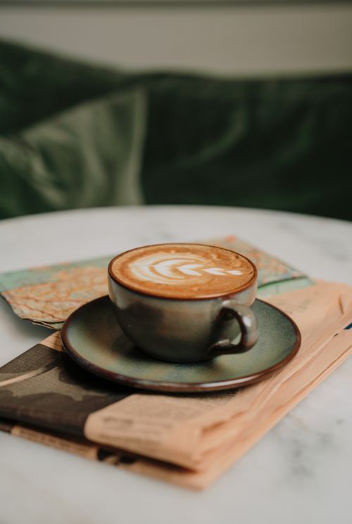 Free A beautifully crafted cappuccino with latte art resting on a newspaper covered table. Stock Photo