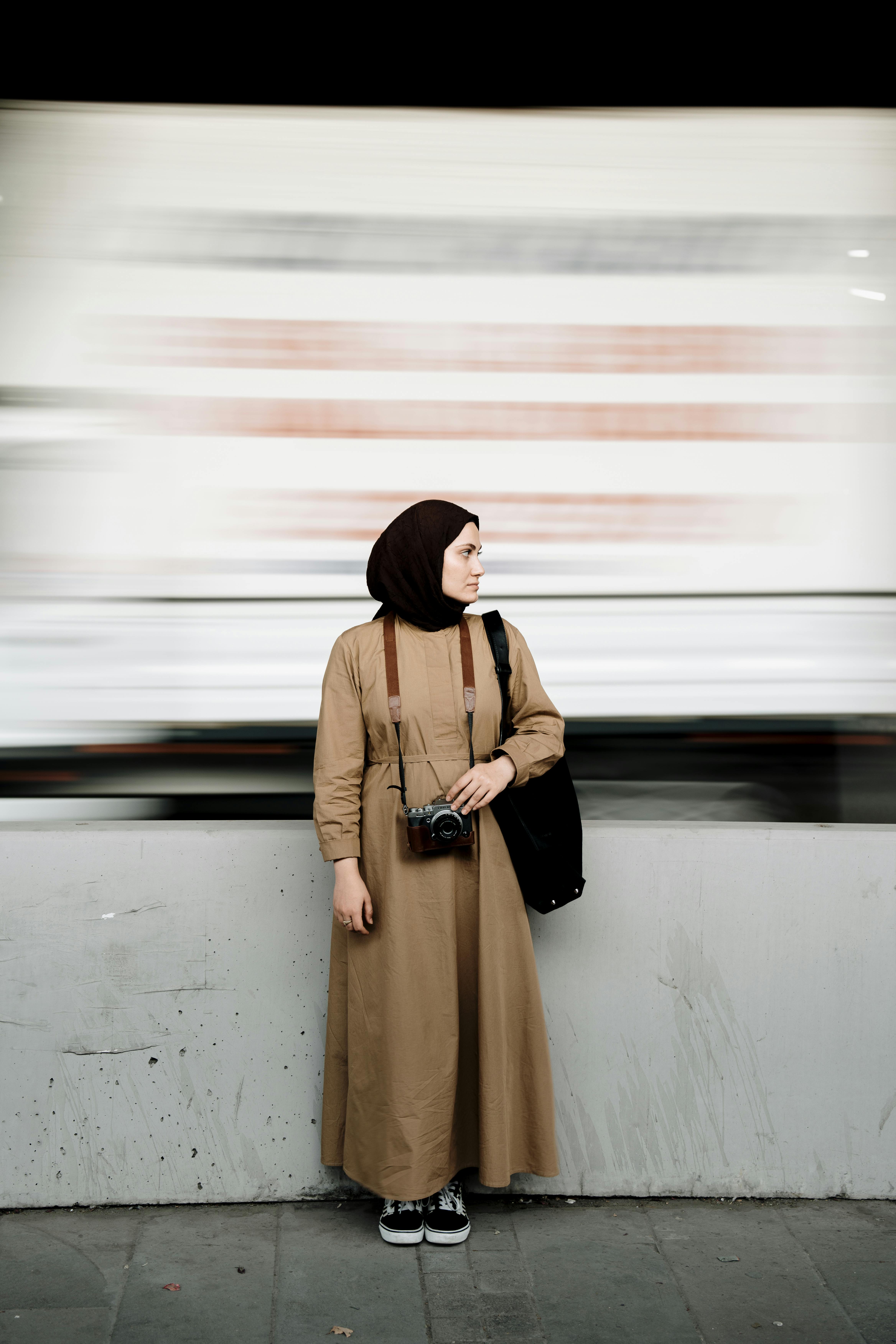 A woman with a headscarf and camera stands in an urban setting in Ankara, Turkey.