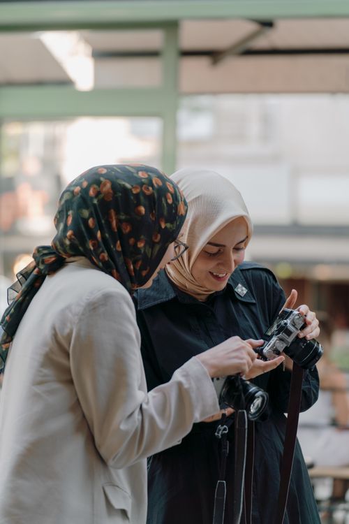 Free Two women in hijabs enjoy a moment sharing a camera on a sunny day in Ankara. Stock Photo