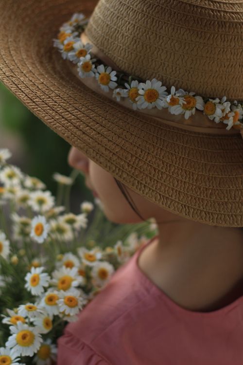 Free A serene portrait of a woman wearing a straw hat adorned with daisies, capturing the essence of summer. Stock Photo