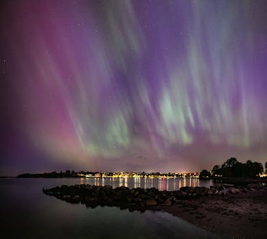 Stunning aurora borealis lights up the night sky over a calm lake in Sønderborg, Denmark.