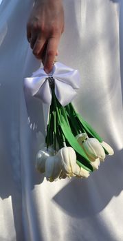 Elegant bride holding a satin-wrapped bouquet of white tulips, perfect for romantic weddings.