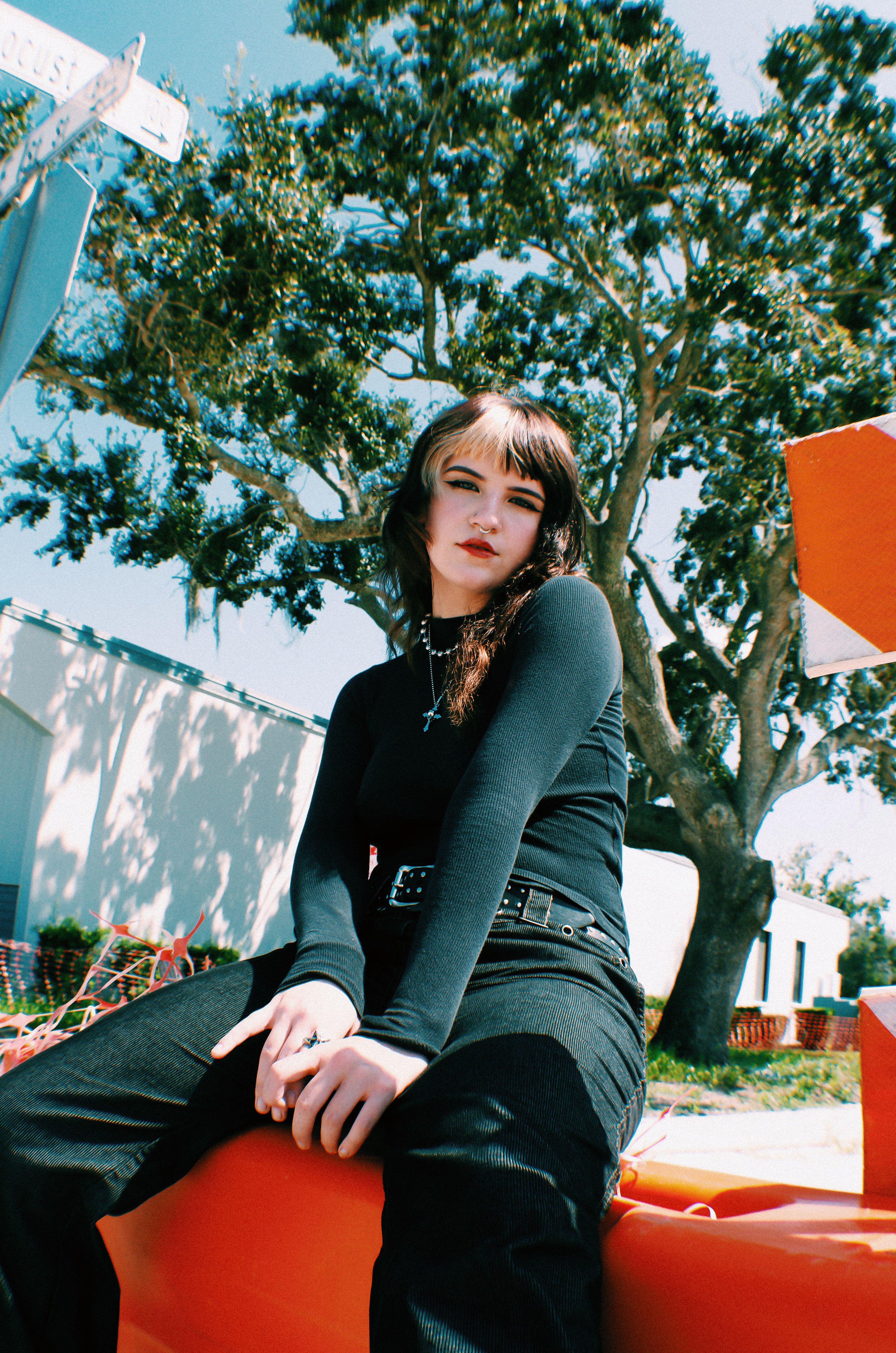 Fashionable young woman in black outfit poses outdoors under a tree, showcasing modern style
