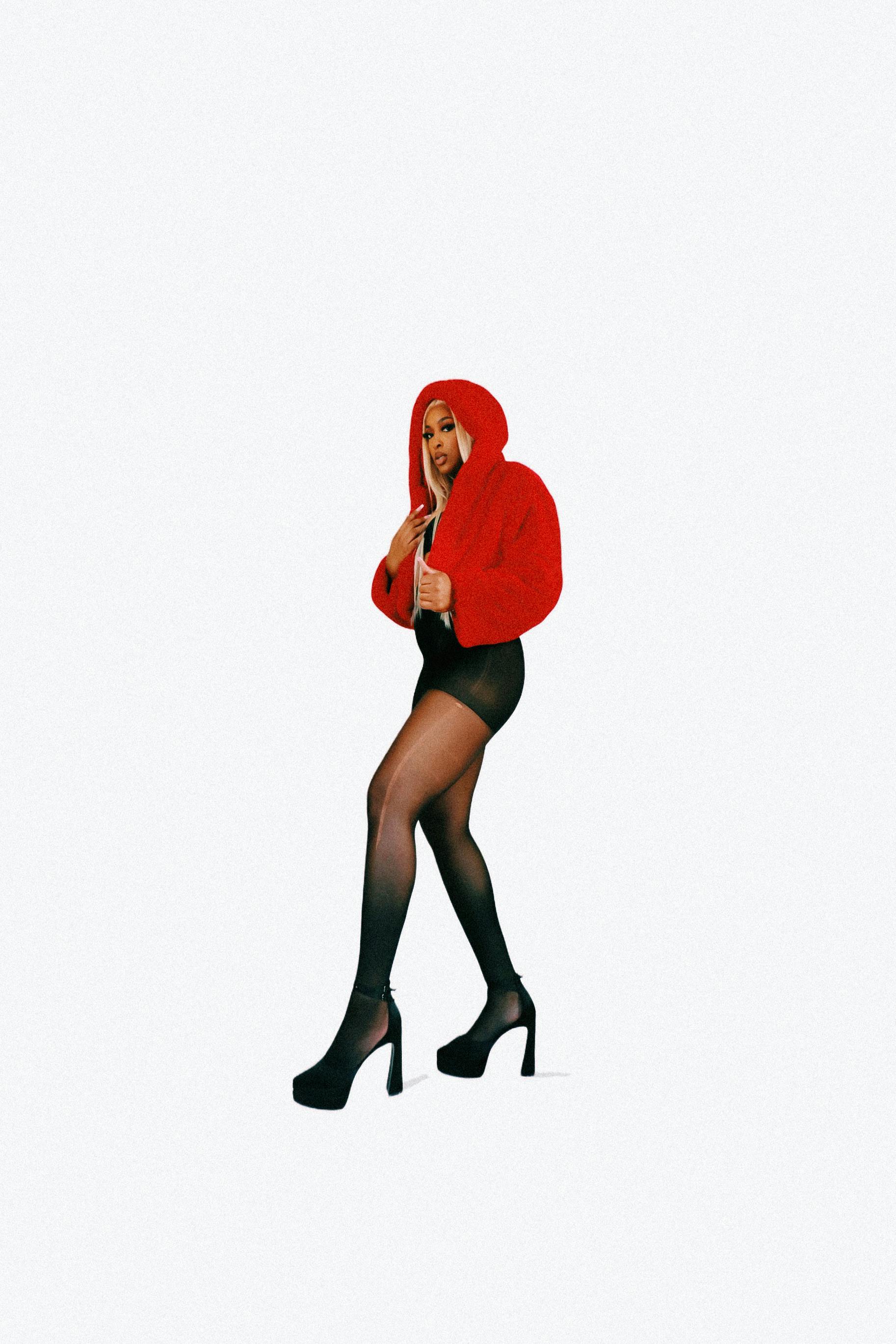 Chic studio photo of a young woman in a red coat and high heels on a white background.