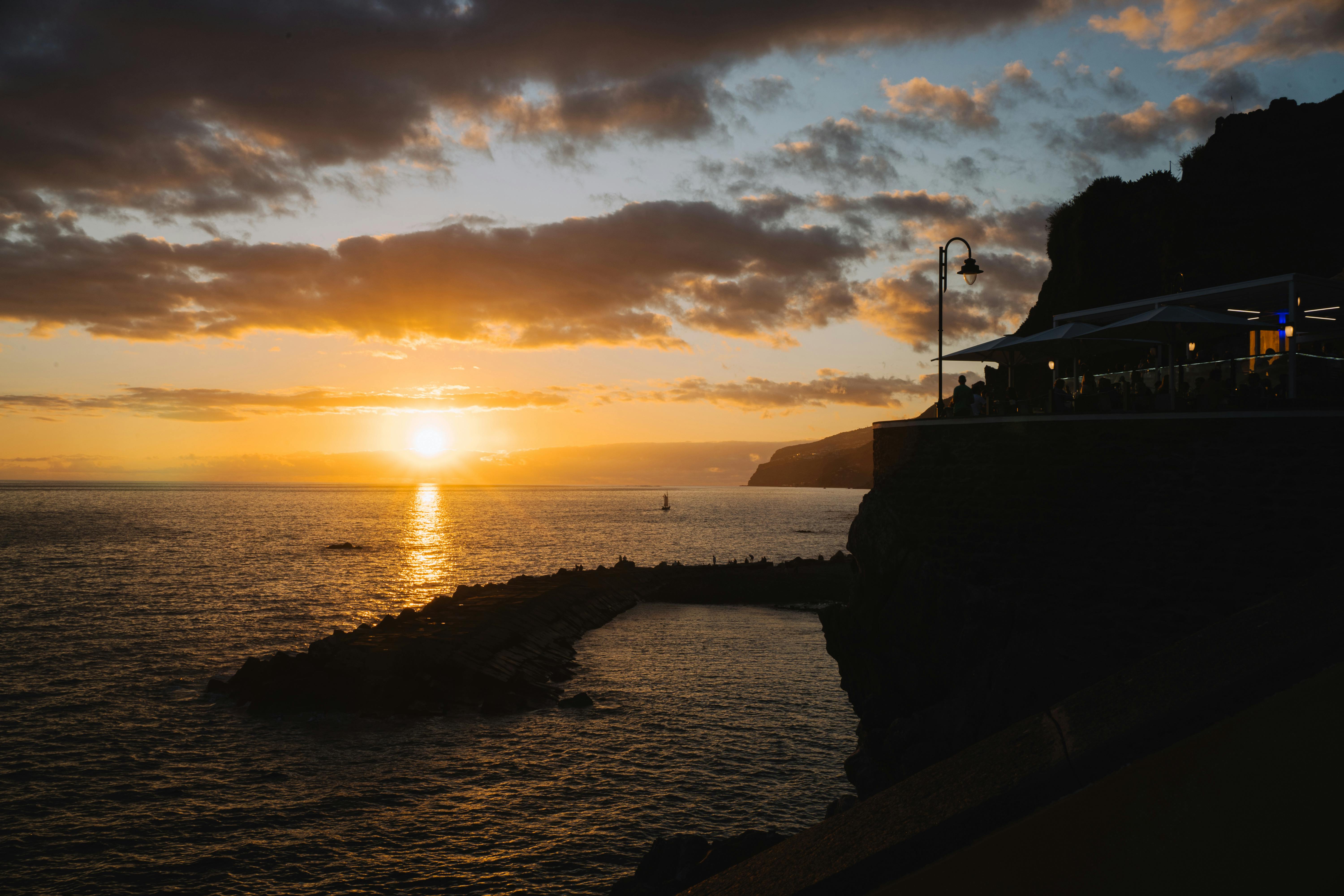A breathtaking sunset over the ocean with a clifftop restaurant silhouetted against the sky.