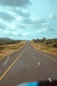 A lonely road stretches through a lush African landscape under a cloudy sky.