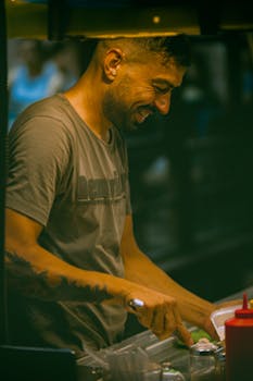 Smiling street vendor preparing food at a bustling night market.