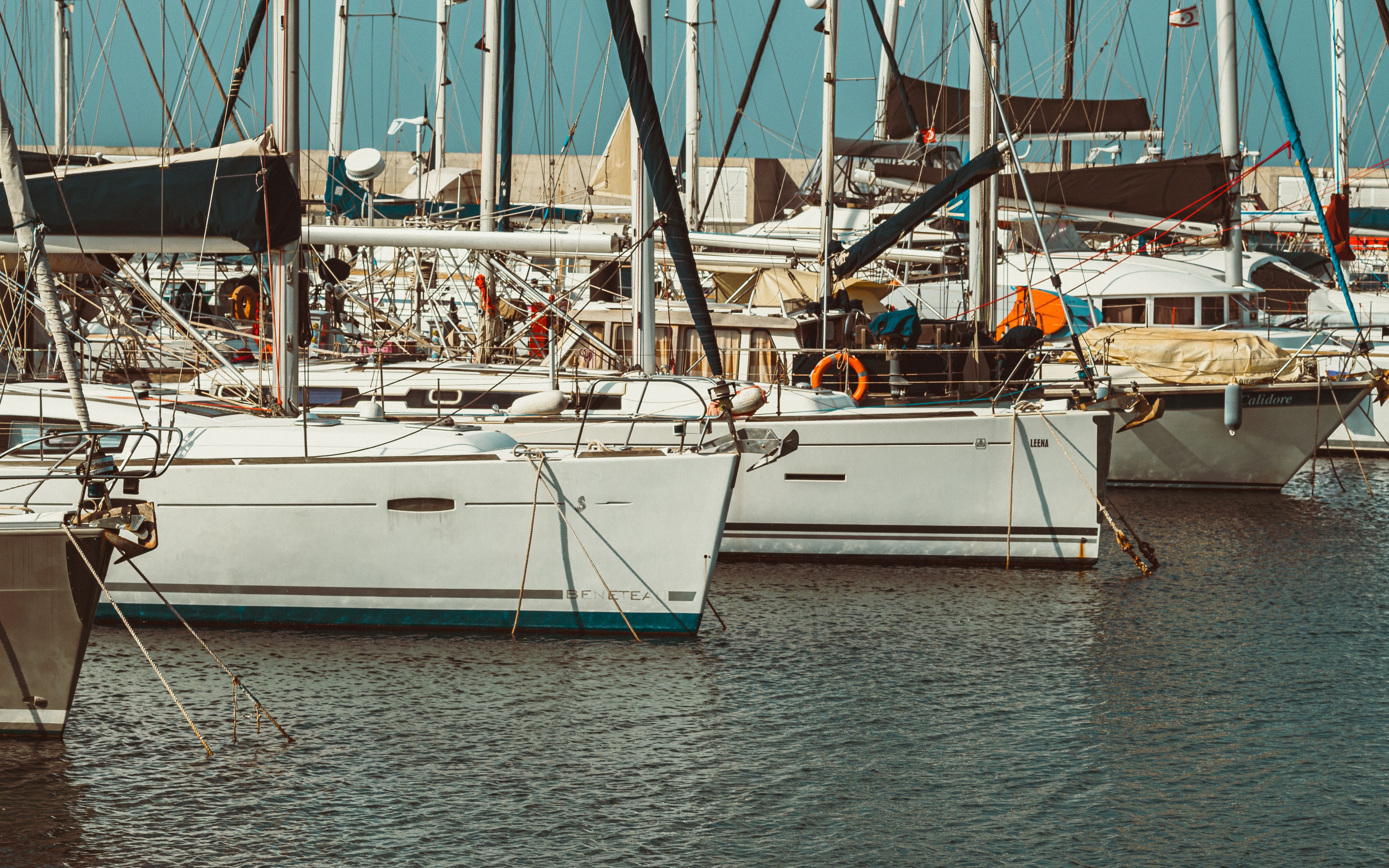 Used boats and yachts docked side by side in a marina under a clear blue sky, Oahu