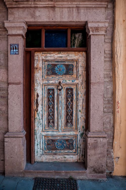 Free A beautifully carved, rustic wooden door with ornate details in a traditional architectural setting. Stock Photo