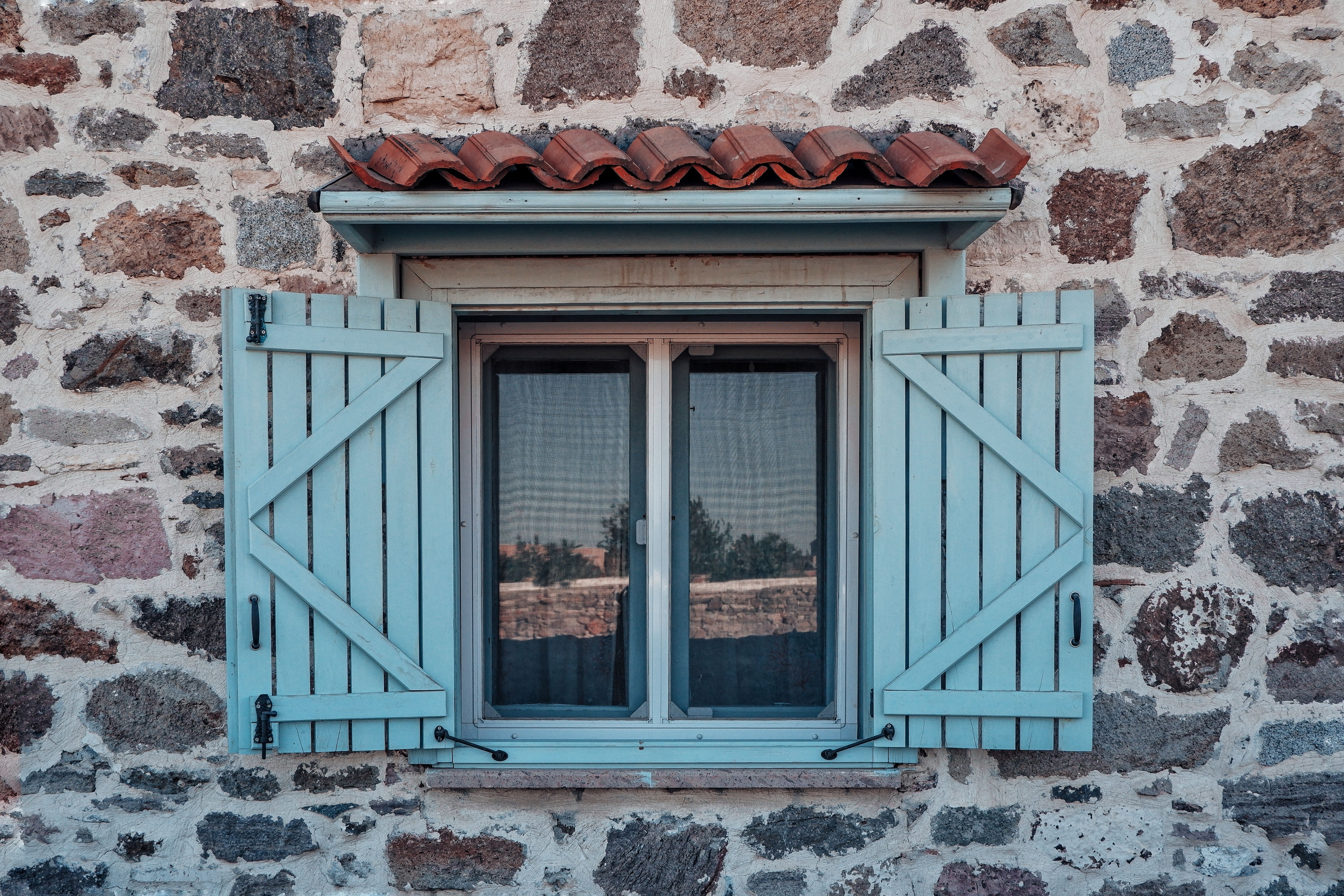 Charming rustic stone house with a blue shuttered window, evoking vintage charm and architectural detail.