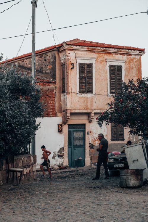 Free A rustic Mediterranean street scene featuring an old house and local residents. Stock Photo