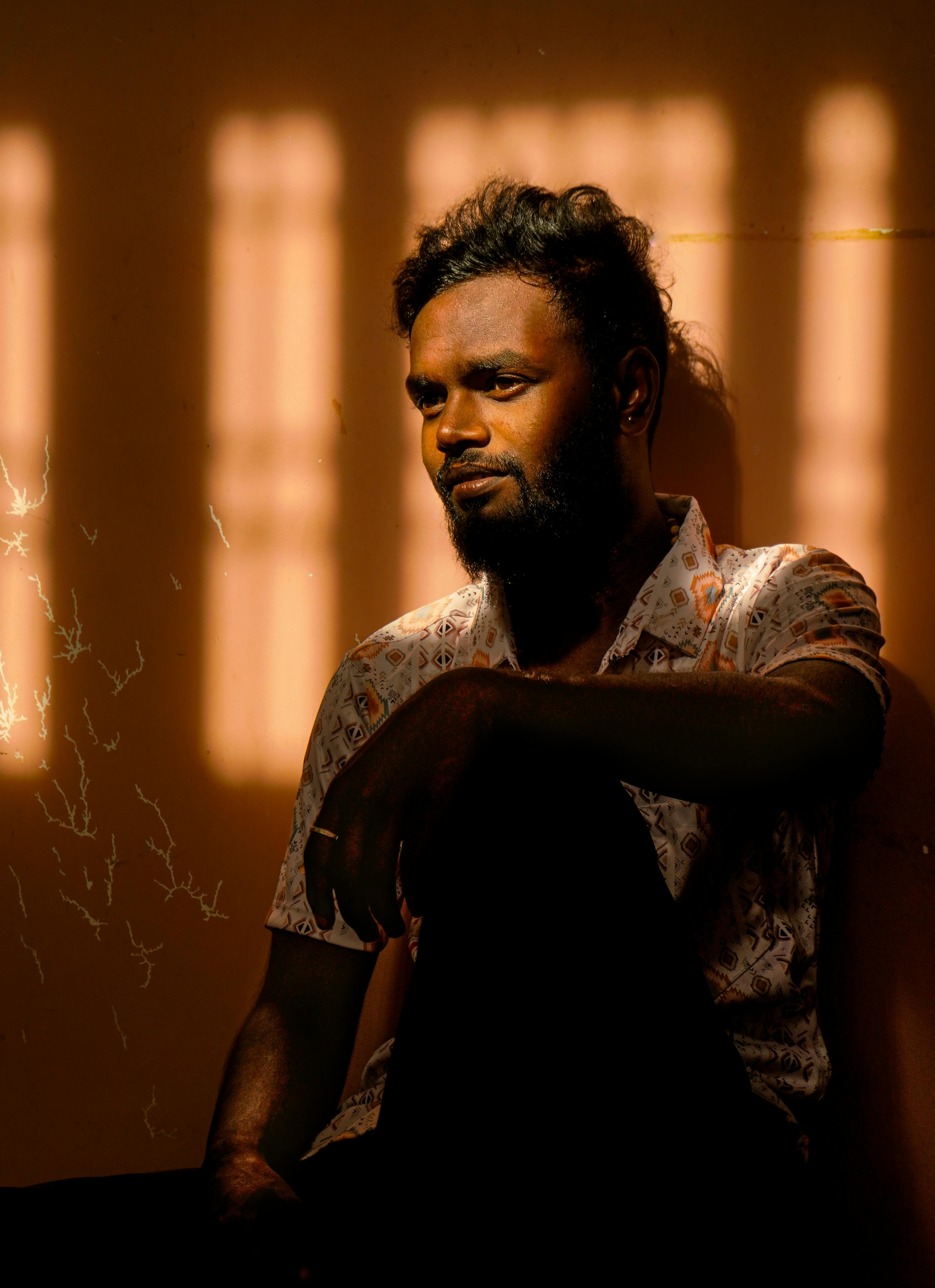 Artistic portrait of a man sitting indoors with dramatic sunlight and shadows.