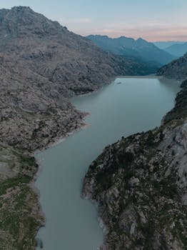 Serene aerial view of a mountain lake surrounded by rugged hills at dusk, offering a tranquil landscape scene.