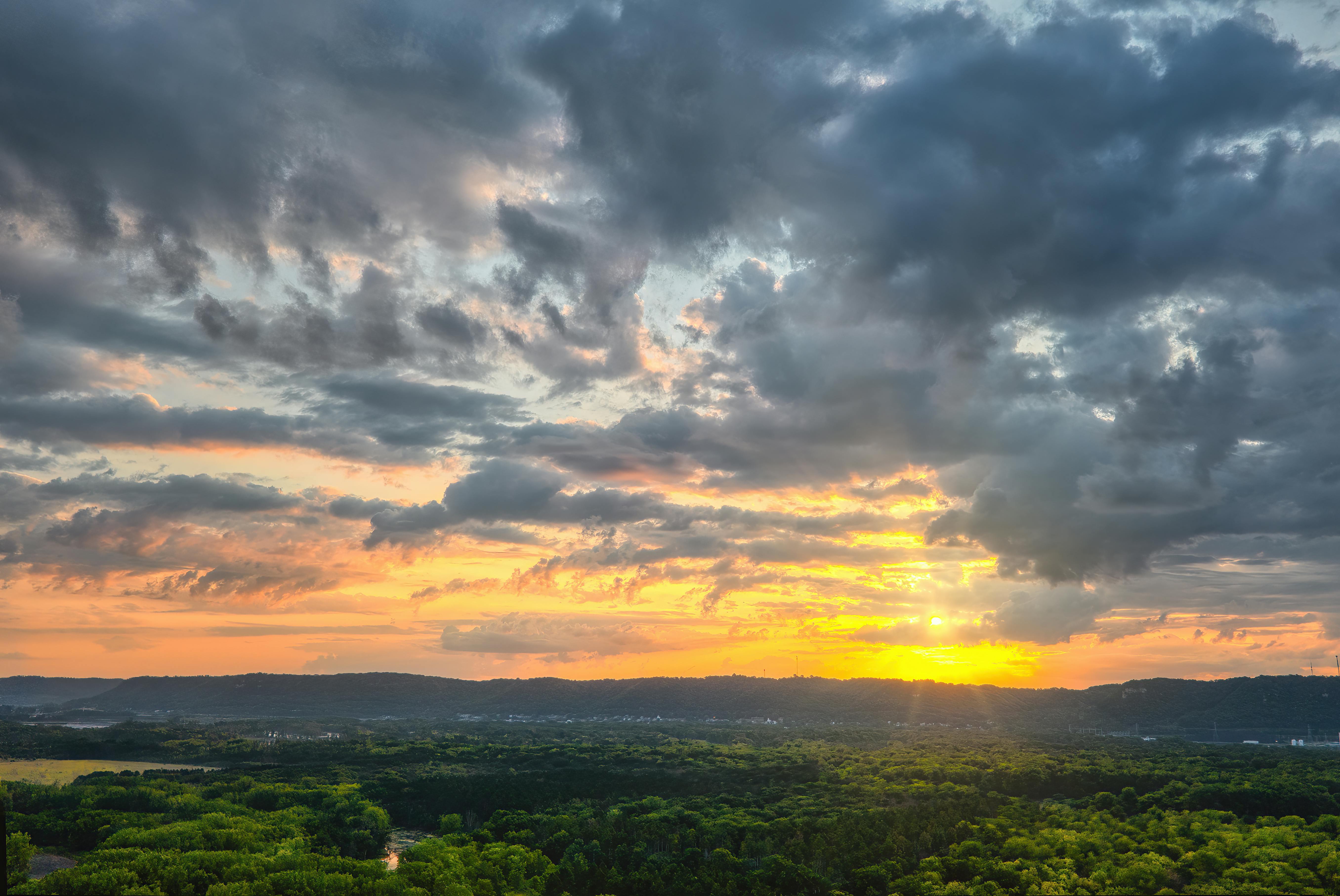 a sunset over a green landscape with trees