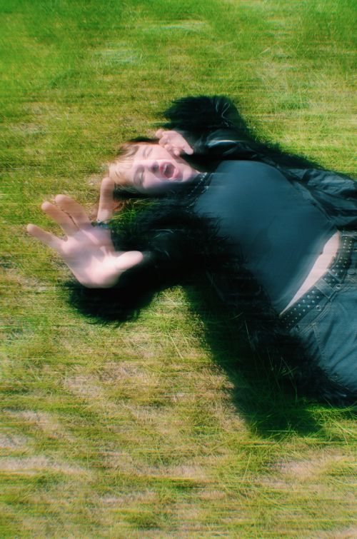 Free A unique artistic portrait of a young adult relaxing on grass outdoors, featuring dynamic motion blur. Stock Photo