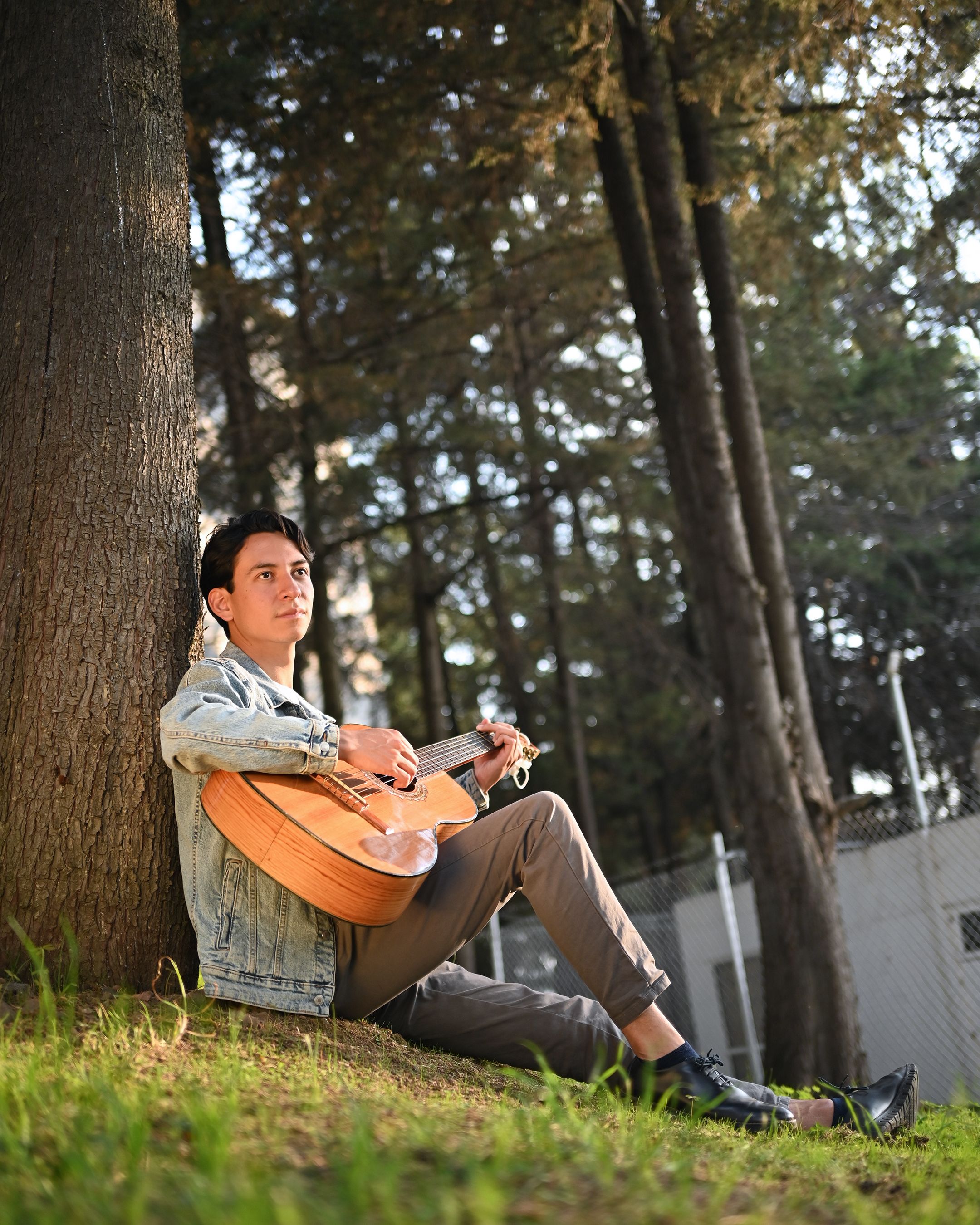 A young man enjoying a peaceful moment playing guitar outdoors in a park.