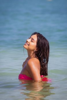 Smiling woman in pink bikini relaxes in the ocean under the sun in Yucatan, Mexico.