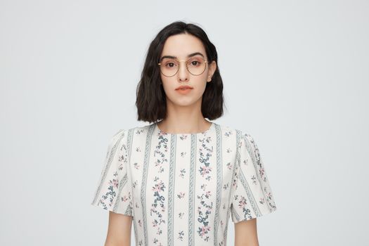 Portrait of a young woman in a floral dress and glasses, studio shot.