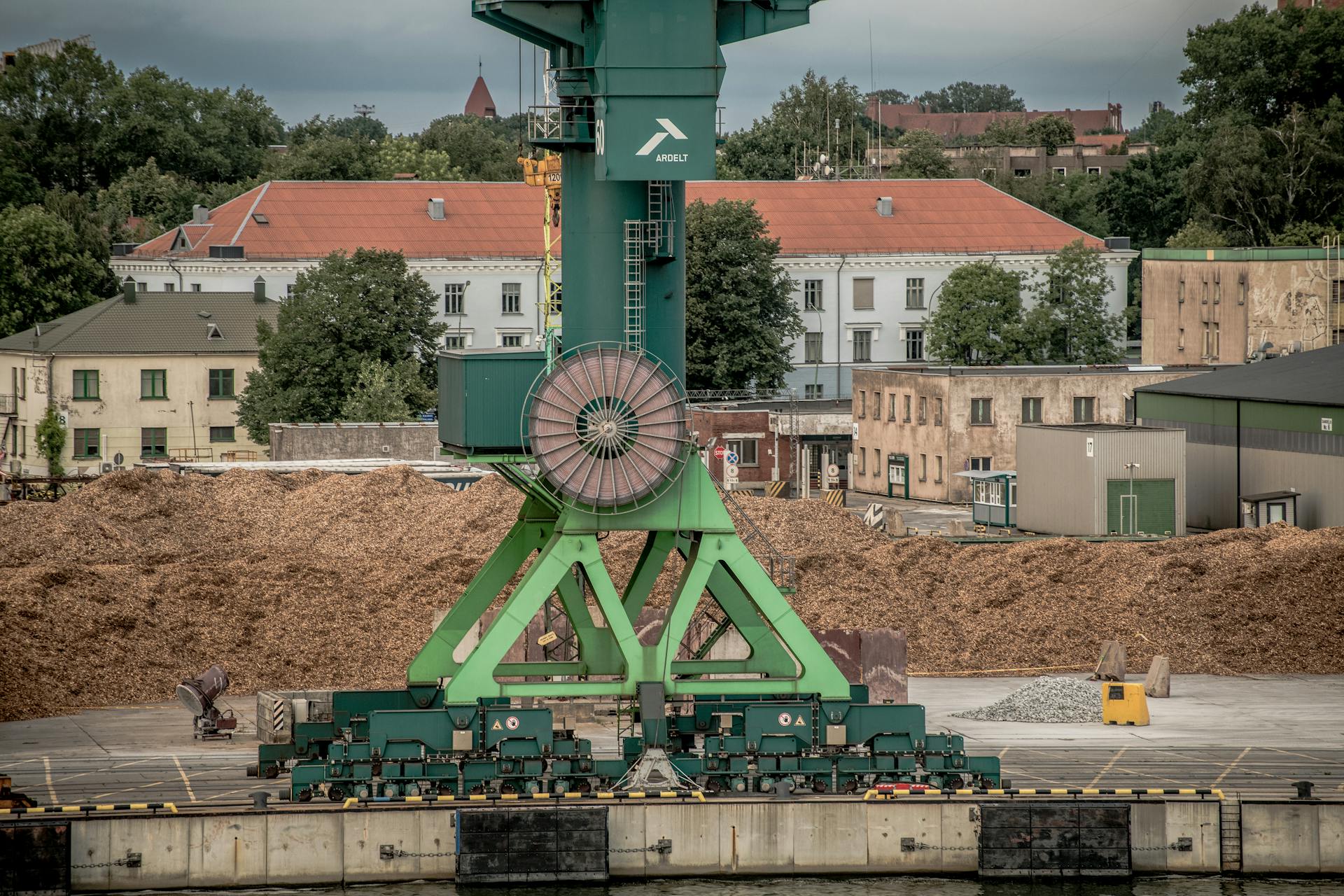A large green industrial crane at Klaipėda Harbor, Lithuania, amidst a backdrop of buildings and trees.