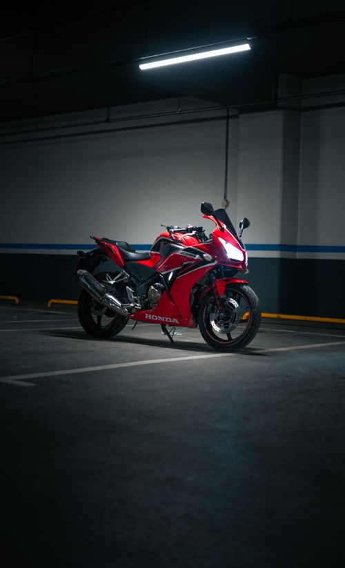 Free A sleek red motorcycle parked in a dimly lit underground parking garage. Stock Photo