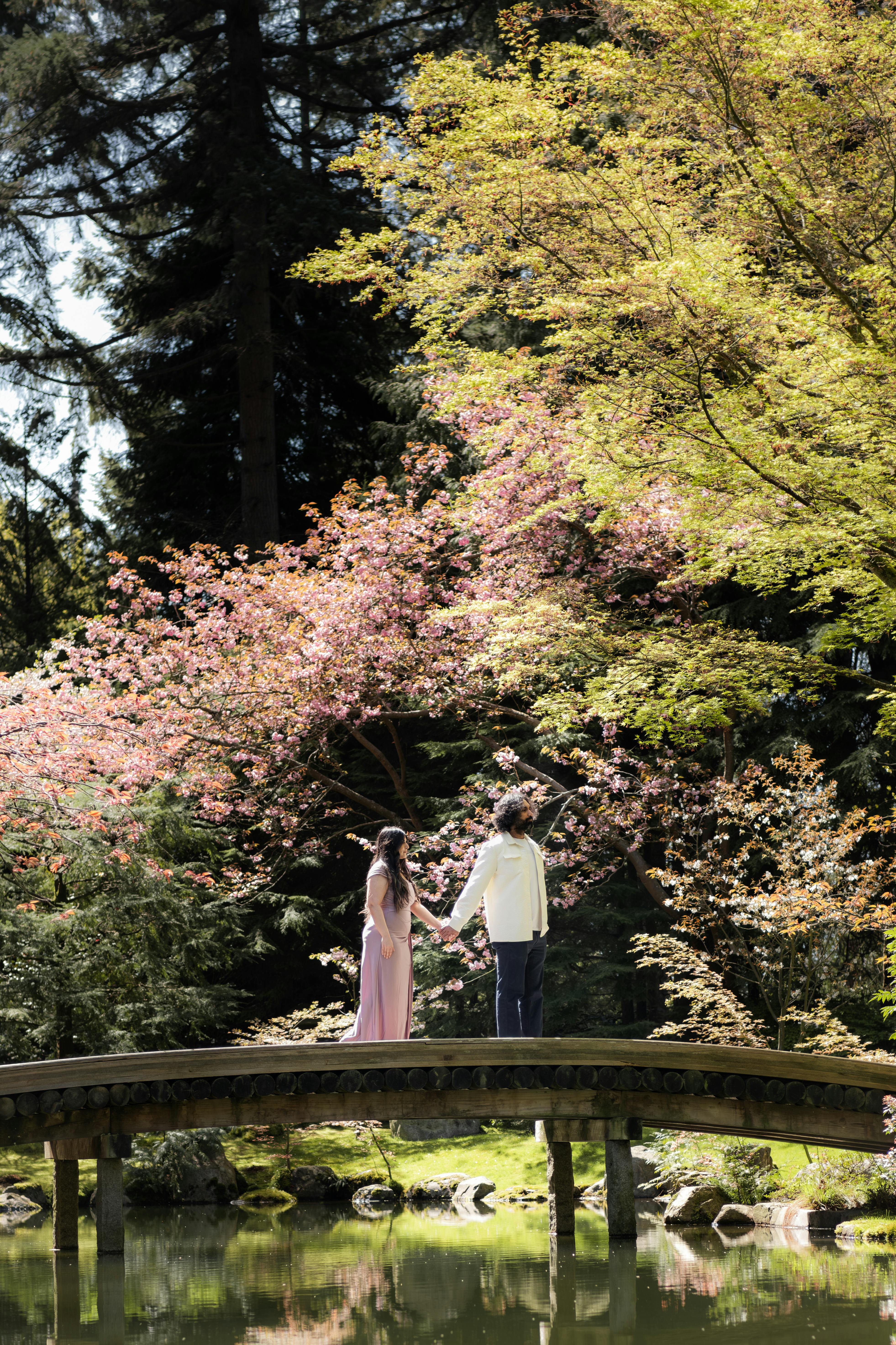 a couple standing on a bridge in the middle of a garden