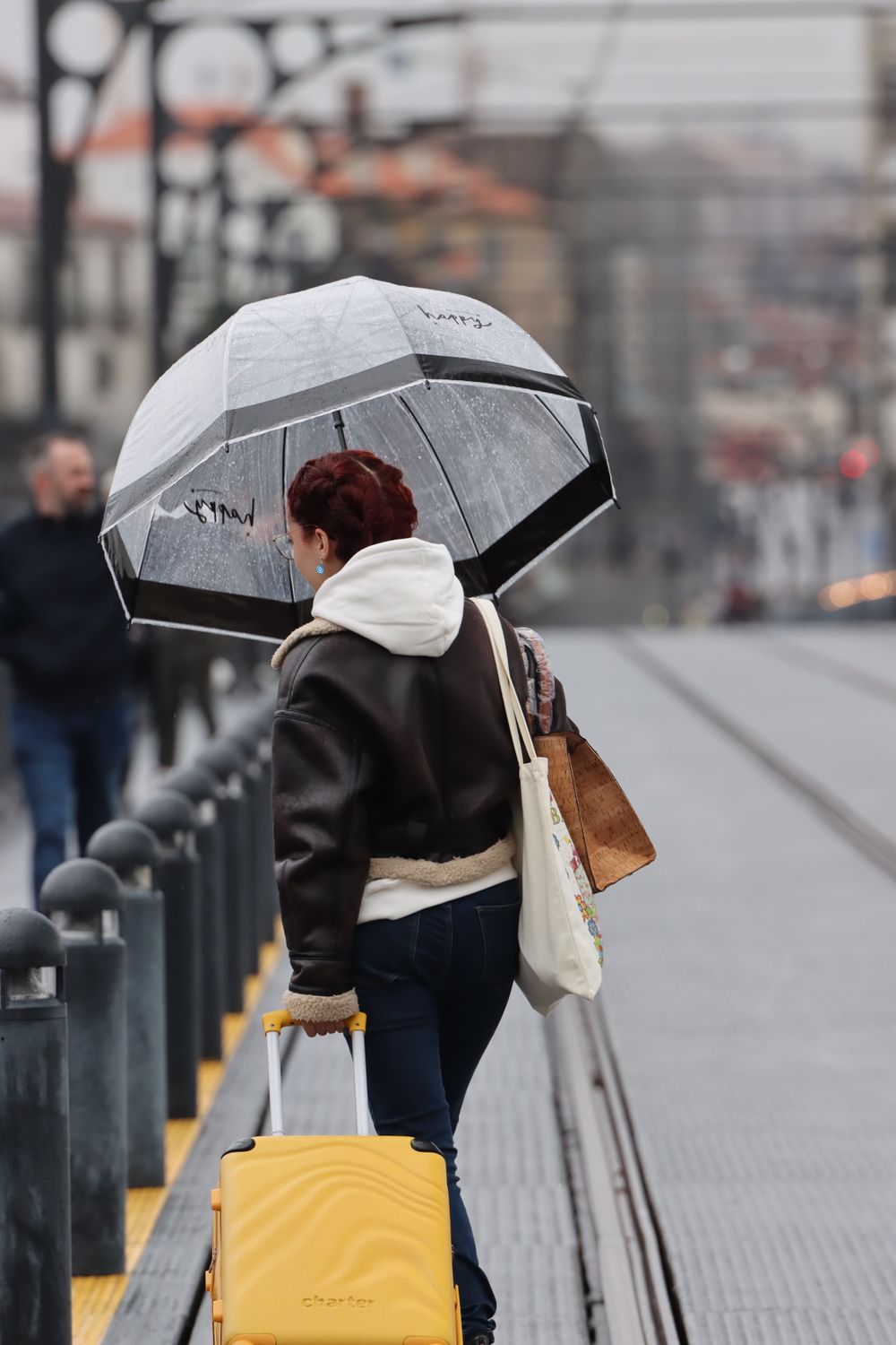 Woman with yellow suitcase walking in rainy Porto under an umbrella