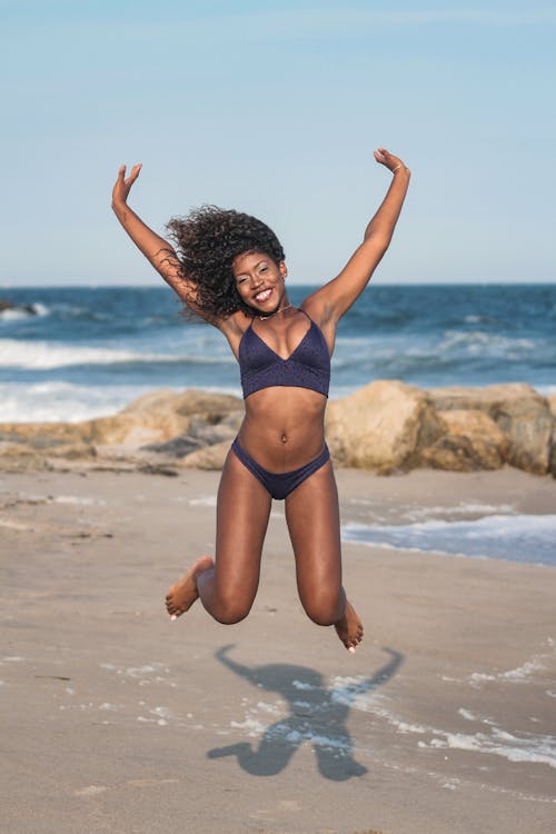 Photo of Happy Woman in Two Piece Bikini Jumping on Shore