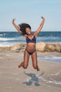 阳光明媚的海滩上，一名穿着泳衣的女子快乐地跳着，浑身散发着幸福感