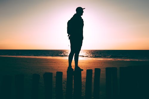 Man Standing On Posts On Seashore During Golden Hour
