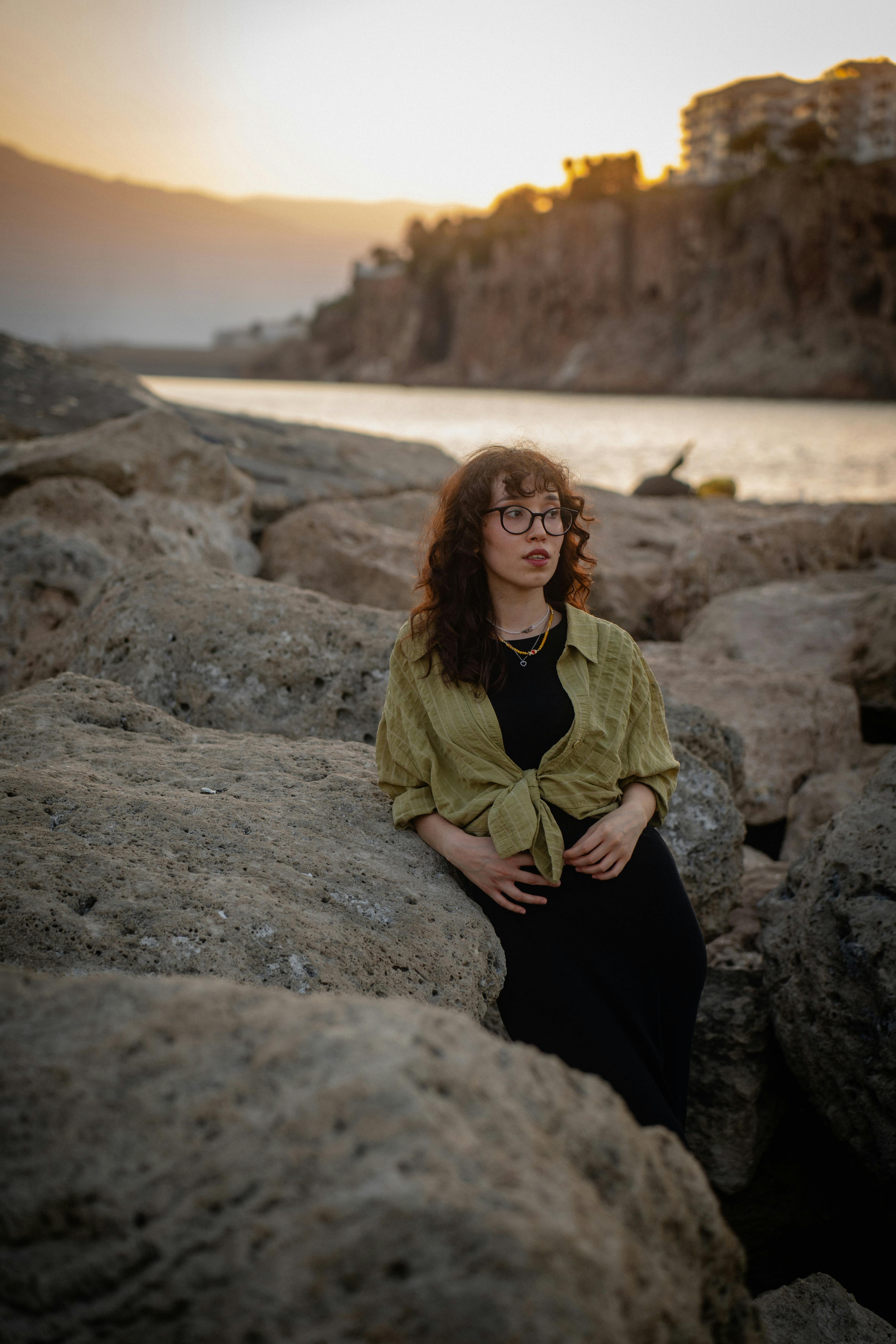 A woman enjoys the calm ambiance of Antalya's rocky coastline during a stunning sunset.