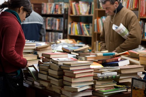 Woman and Man Standing Beside Piles of Books
