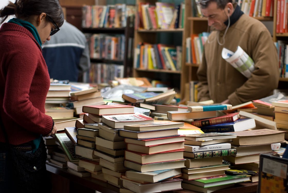 Free Woman and Man Standing Beside Piles of Books Stock Photo