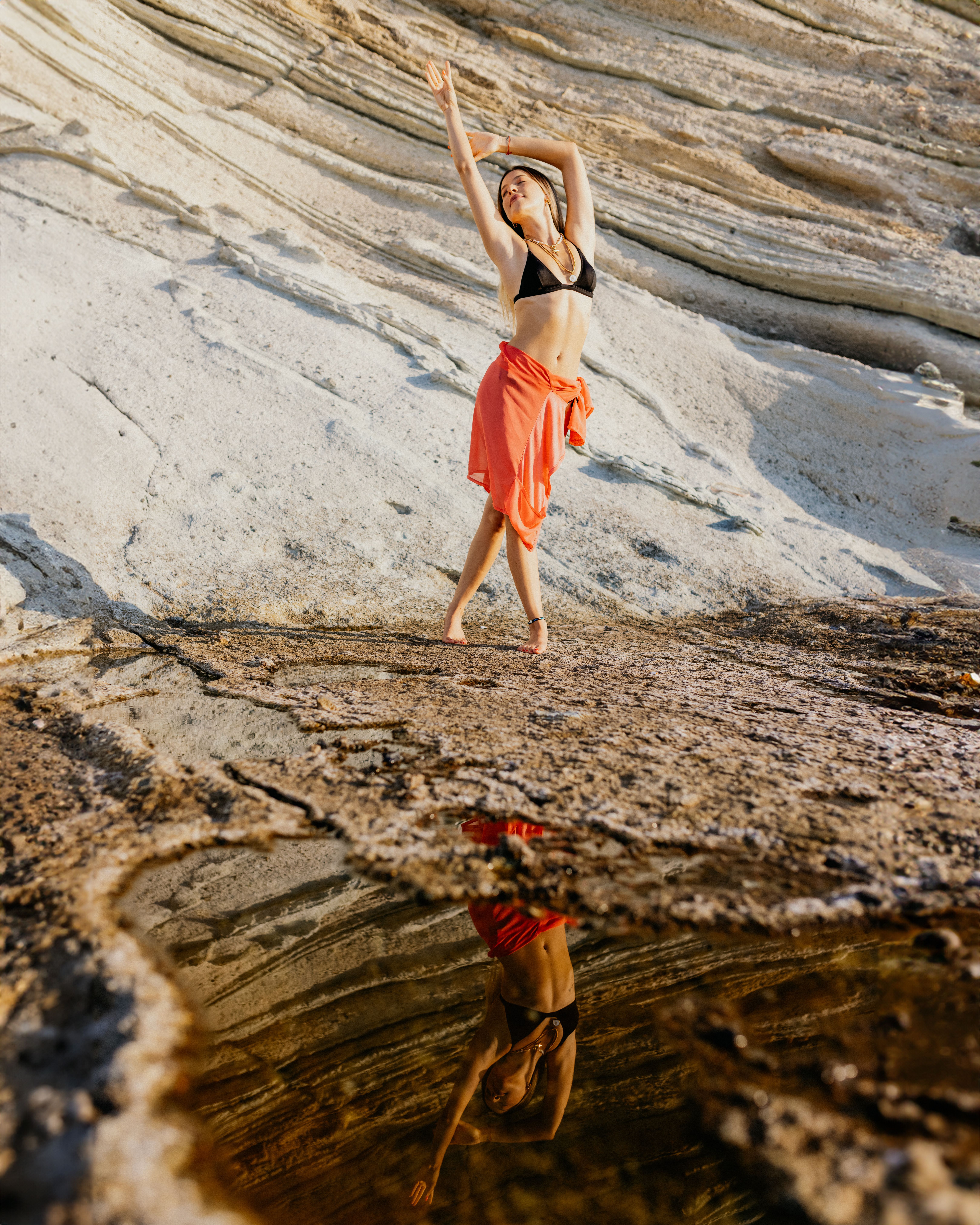 A woman in a red dress is standing in front of a rock · Free Stock Photo
