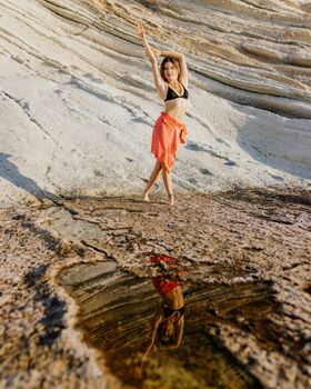 A woman in beachwear reflects by water on a rocky shore, enjoying the summer outdoors.