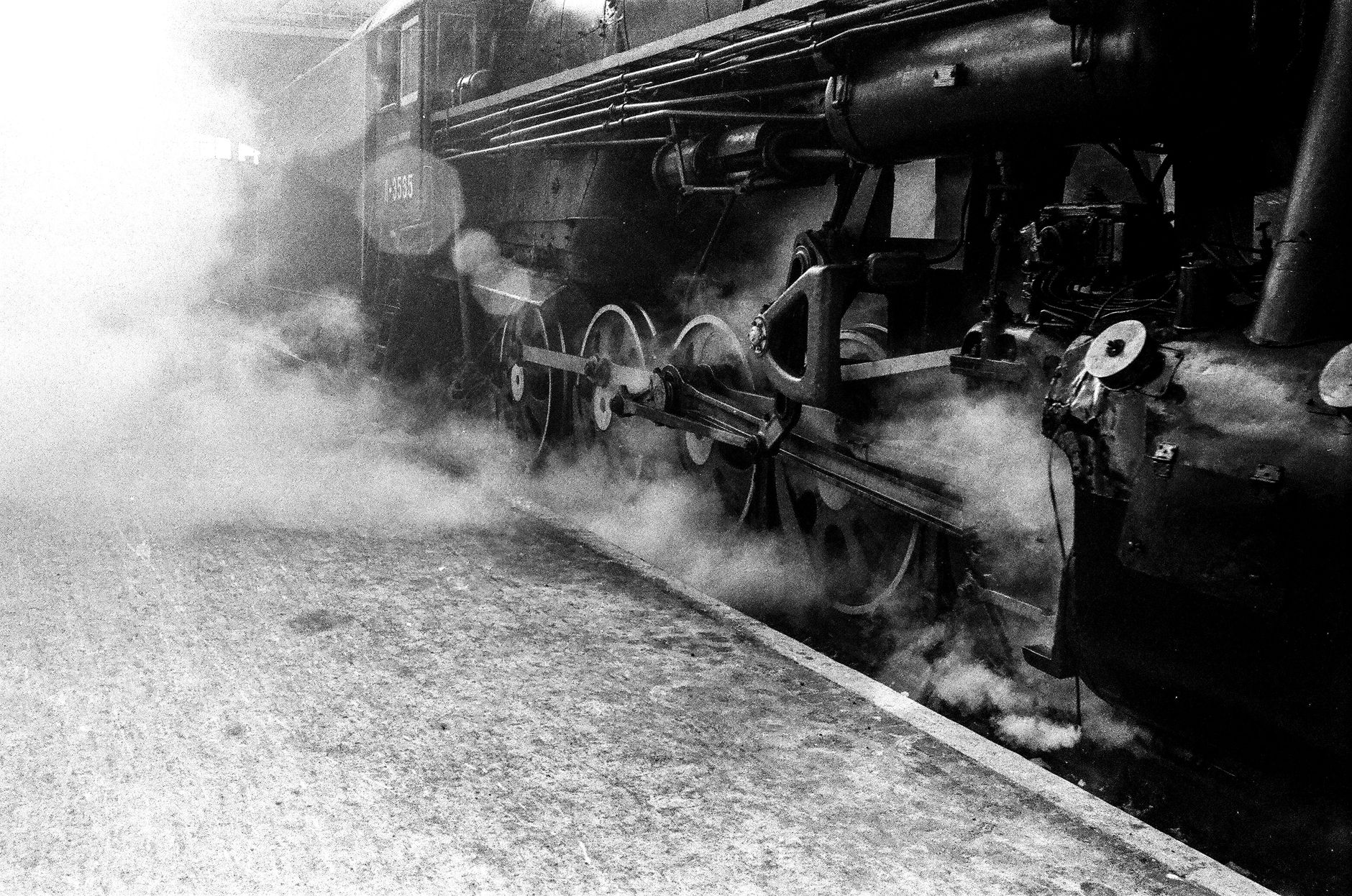 Monochrome photo of a steam locomotive releasing smoke at a train station. — free online jigsaw puzzle on JigsawPuzzlesFreeOnline.org