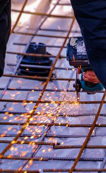 A construction worker skillfully cuts steel with an angle grinder, creating flying sparks outdoors.