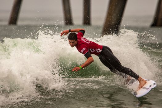 Surfer skillfully rides the waves in a powerful display of surfing near a pier.