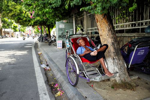 Free An elderly man relaxes in a cyclo on a shaded street in Hue, Vietnam, capturing daily urban life. Stock Photo