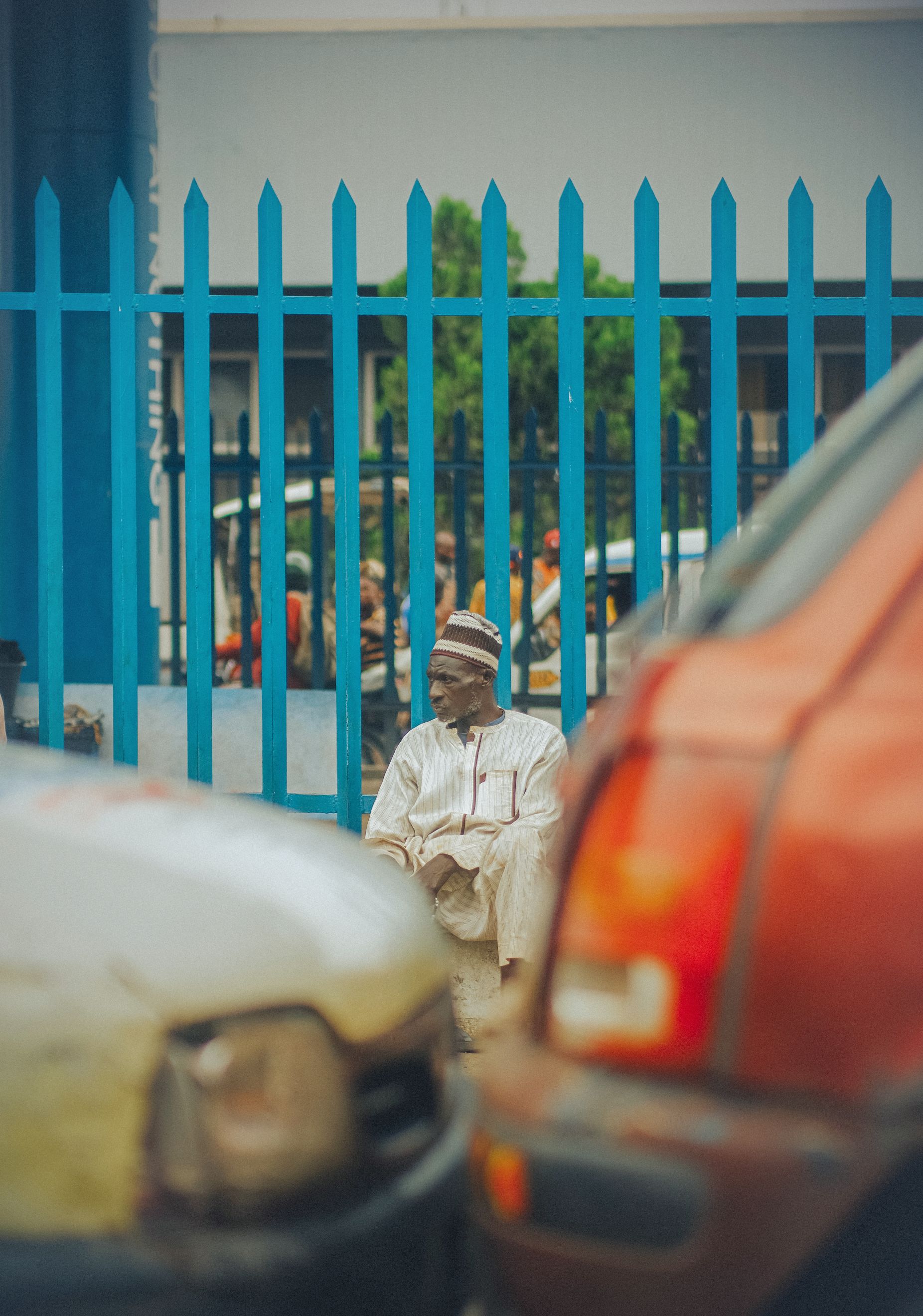 A man in traditional attire sits near traffic in Ibadan, Nigeria, showcasing vibrant city life.