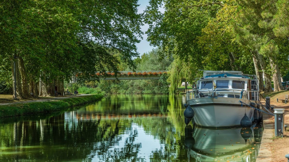 A canal boat moored under shade trees on a quiet French canal