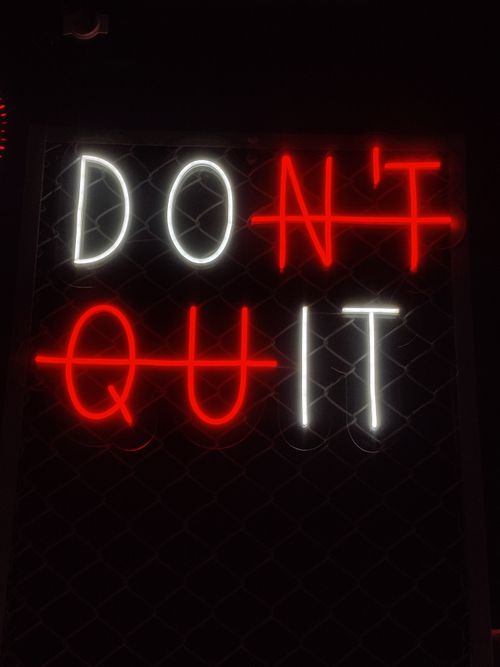 Free Illuminated 'Don't Quit' neon sign with motivational message in a dark background. Stock Photo