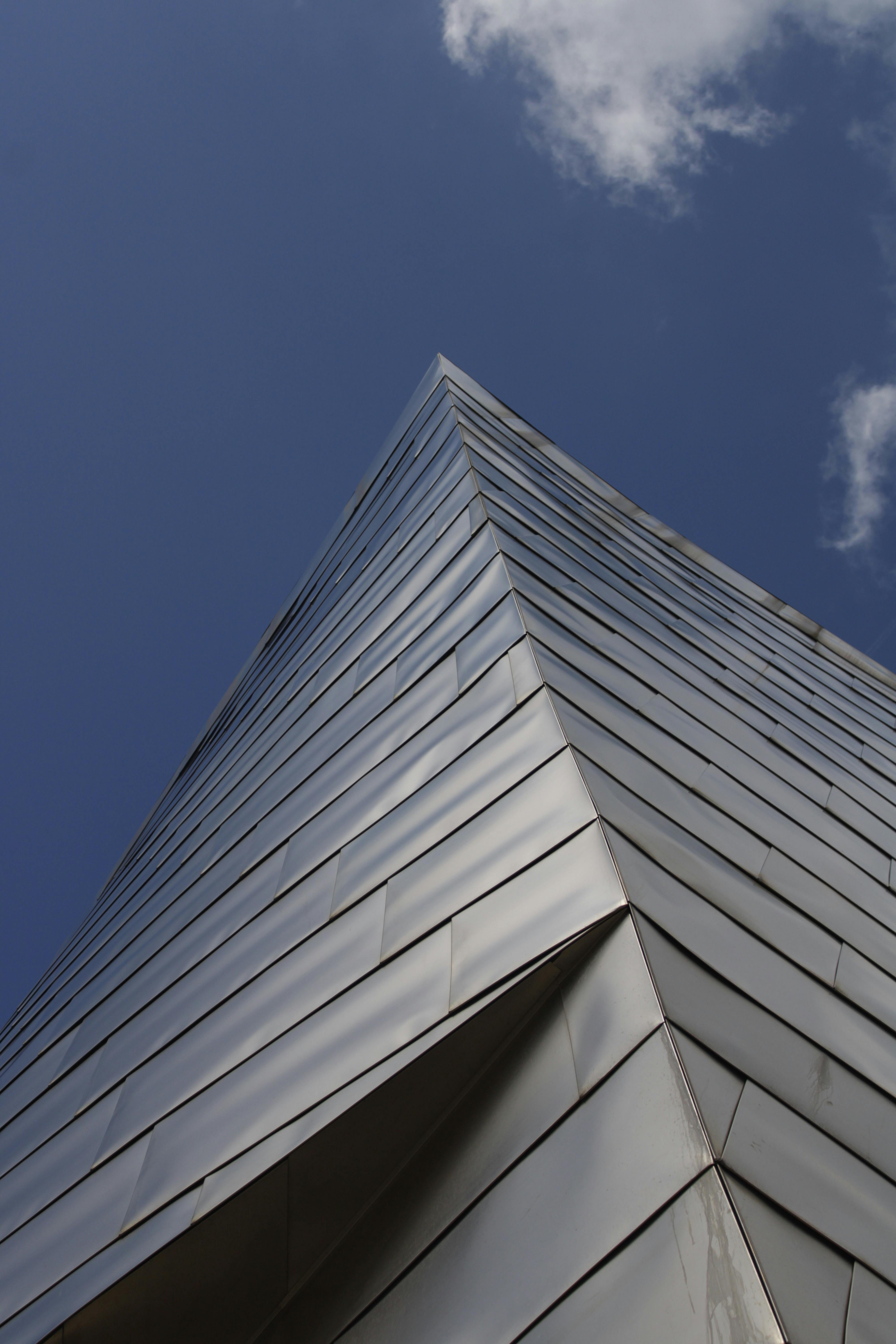 Angular perspective of a modern skyscraper with reflective metal facade against a blue sky.