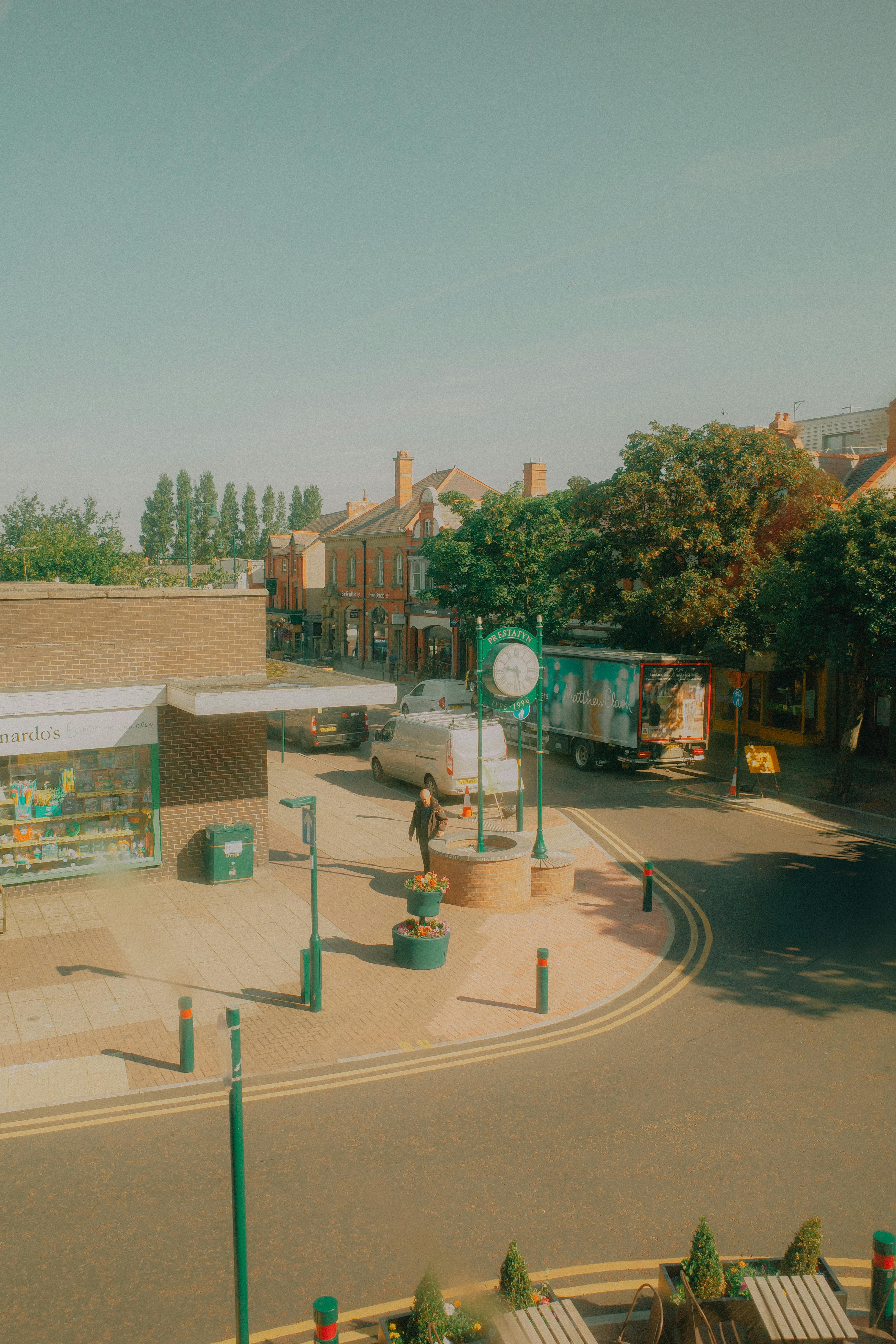 Clear sunny view of a street in Prestatyn, Wales showcasing buildings, people, and vehicles.