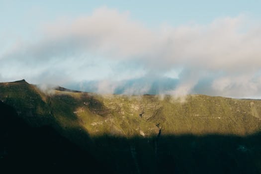 Majestic view of a lush mountain range with clouds at sunrise, showcasing nature's beauty.